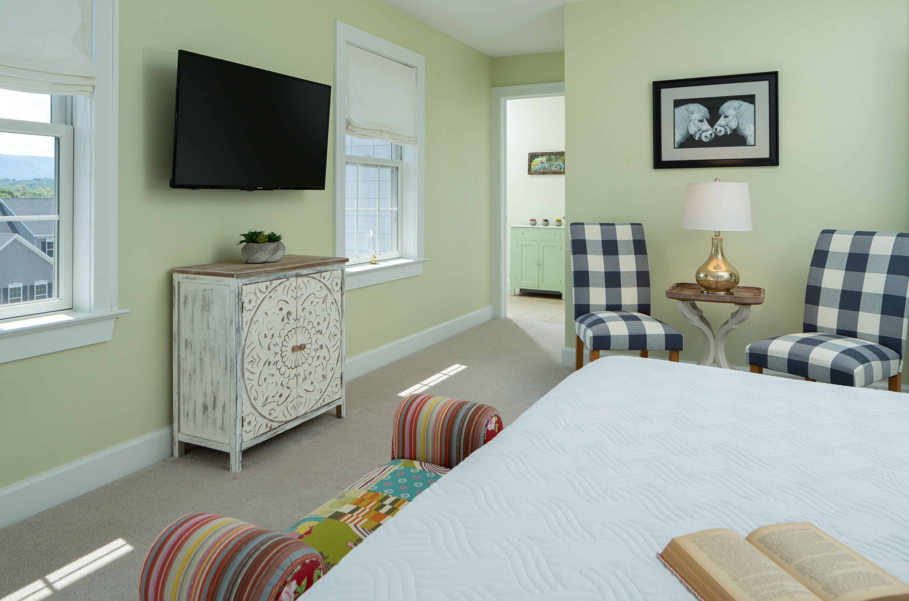 A bedroom with a bed, a television, a dresser, two chairs, a lamp, and a framed picture on the wall.