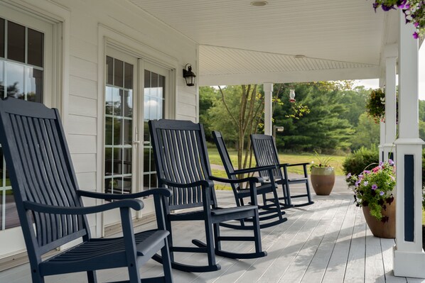 A porch with three rocking chairs and a large planter with flowers. - Apple Pony Inn (Boalsburg)