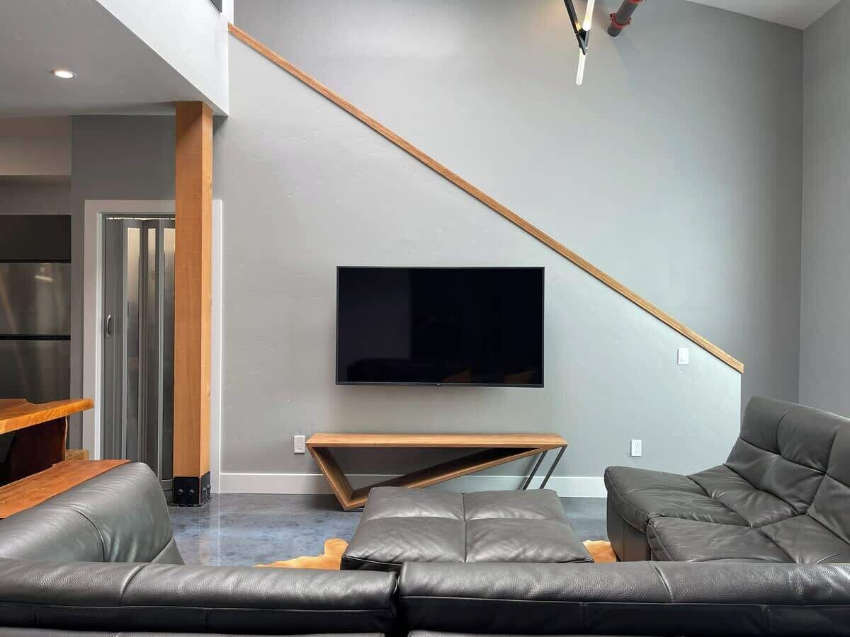 Un salon moderne avec un grand téléviseur à écran plat fixé au mur, une table basse en bois et un canapé en cuir gris.