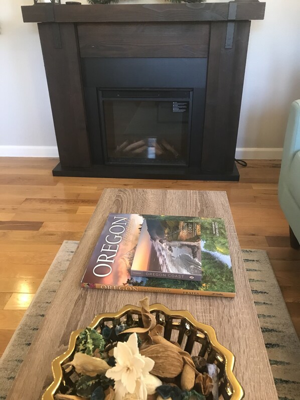 A book titled "Oregon Coast" on a wooden coffee table in front of a fireplace. - Charming Parkside Bungalow-2 blocks from downtown! (Silverton)