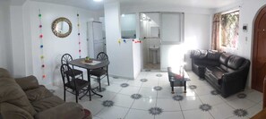 A living room with a sofa, a dining table with chairs, a coffee table, a black leather couch, a kitchen area with a refrigerator, and a bathroom with a sink and mirror. - Departamento Familiar y Céntrico con Patio (Cusco)