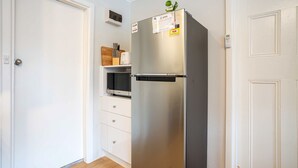 A compact kitchen with a stainless steel refrigerator, a microwave, and a white cabinet with a knife block.