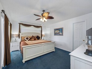 A bedroom with a bed, a ceiling fan, a nightstand, a lamp, a painting, and a door. - Oasis Key Retreat (10 mins from Disney) 75" TV | Private Pool | Game Room (Kissimmee)
