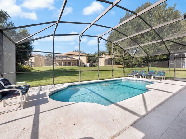 A covered outdoor swimming pool with lounge chairs and a view of houses in the background. - Oasis Key Retreat (10 mins from Disney) 75" TV | Private Pool | Game Room (Kissimmee)