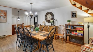 A dining area with a wooden table and chairs, a chandelier, a clock, and a bookshelf with books and games. - 1 Mi to Downtown Conway: Spacious Family Condo! (North Conway)