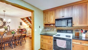 A kitchen with wooden cabinets, a microwave, an oven, and a dining area with chairs and a table. - 1 Mi to Downtown Conway: Spacious Family Condo! (North Conway)