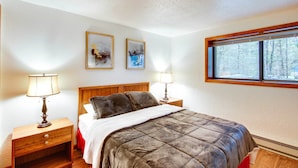 A bedroom with a bed, two bedside tables with lamps, a window with a view of trees, and two framed pictures on the wall. - 1 Mi to Downtown Conway: Spacious Family Condo! (North Conway)