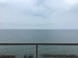A view of the sea from a balcony with a railing, a rocky shoreline, and a cloudy sky. - 2BR/2BA LAKEFRONT CONDO 305 Private Beach/Balcony/indoor pool. (Geneva)