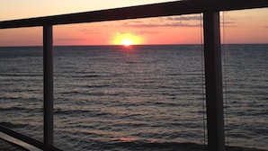 Sonnenuntergang über dem Meer, betrachtet vom Balkon mit Geländer.