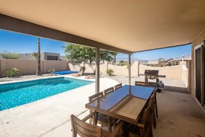 A covered patio with a pool, wooden table and chairs, and a barbecue grill. - “THE SANDY WAKE”Desert Oasis Sleeps 8 with a pool (Lake Havasu City)