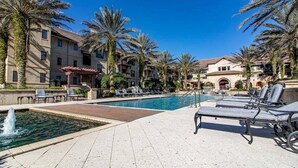 A pool area with lounge chairs, palm trees, and a building with balconies.