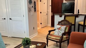A living room with a coffee table, a sofa, a patterned rug, and a chair with a cushion.