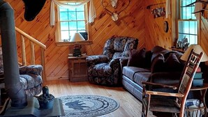 Interior rústico de una cabaña con techo de madera, chimenea, sofá y mesa de comedor.