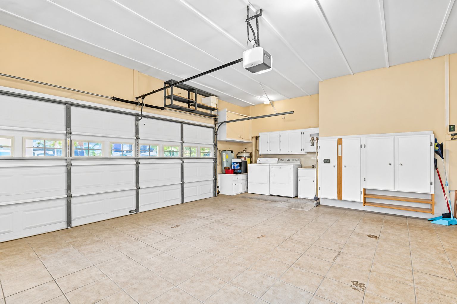 Een ruime garage met een grote witte deur, een projector aan het plafond en een wasruimte met wasmachines.