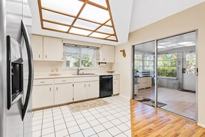 Une cuisine moderne avec des meubles blancs, un lave-vaisselle noir et une grande fenêtre.