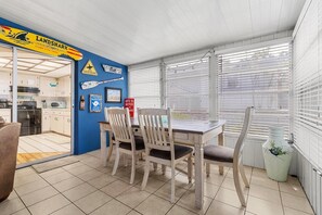 A dining area with a table and chairs, a potted plant, and a kitchen visible through an open door.