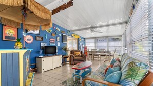 A spacious living area with a blue wall, a wooden sofa, a TV, and a dining table. - Vibrant Tropical Escape – Just Minutes from the Beach + Serene, Fenced Yard! (Largo)