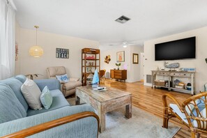 A living room with a sofa, armchair, coffee table, and a TV on a wall.