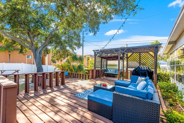 A wooden deck with outdoor furniture, a pergola, and a view of a residential area.