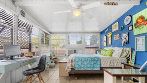 A room with a bed, desk, and chair, a ceiling fan, and a window with blinds. - Vibrant Tropical Escape – Just Minutes from the Beach + Serene, Fenced Yard! (Largo)