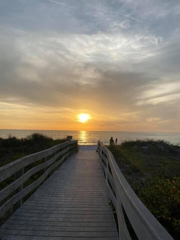 A wooden boardwalk leading to the ocean with a sunset in the background.