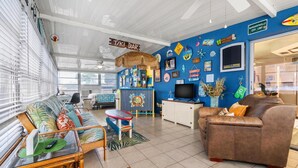 A room with a sofa, a small table, a TV, and a sign that reads "TIKI BAR". - Vibrant Tropical Escape – Just Minutes from the Beach + Serene, Fenced Yard! (Largo)