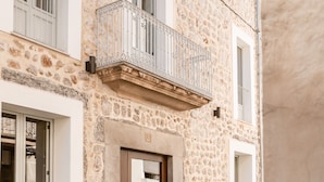 A stone building with a wooden door, a balcony with metal railings, and a small sign above the door. - Meem Townhouse (Sóller)