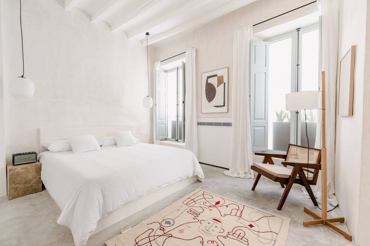 A minimalist bedroom with a large bed, a bedside table, a chair, and a floor lamp.