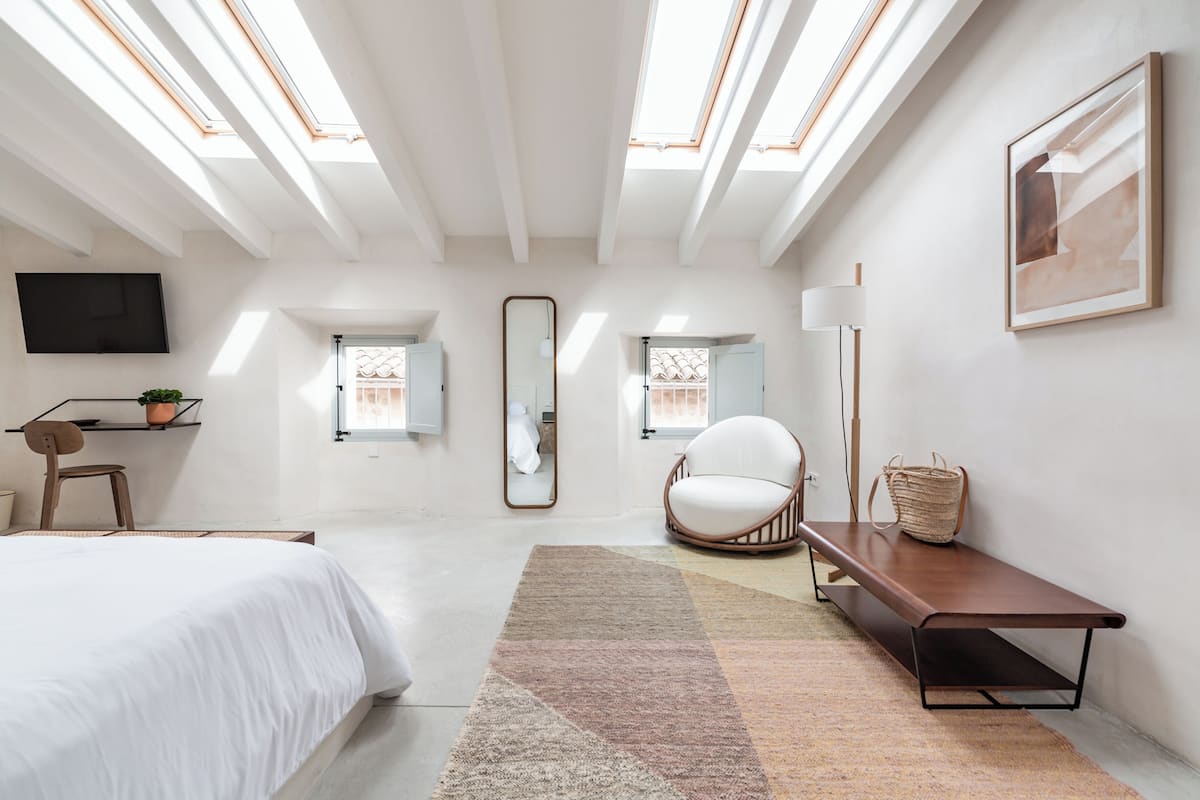 A modern bedroom with skylights, a bed, a chair, a bench, and a mirror.