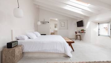 Un dormitorio moderno con una cama grande, un escritorio, una silla y un televisor en la pared.