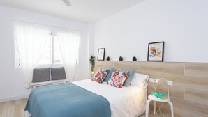 A bedroom with a bed, a bedside table, a chair, a ceiling fan, and a wall with framed pictures.