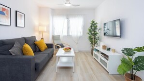 A modern living room with a grey sofa, a white coffee table, a white TV stand, and a ceiling fan.