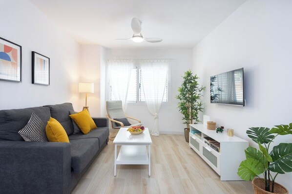 Ein modernes Wohnzimmer mit einem grauen Sofa, einem weißen Couchtisch, einer weißen TV-Konsole und einem Deckenventilator.