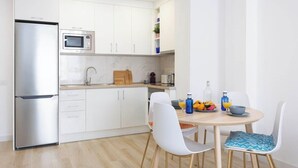 A modern kitchen with white cabinets, a stainless steel refrigerator, a microwave, and a dining area with white chairs and a round table.