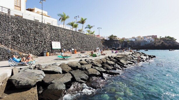 A coastal area with a rocky shoreline, a stone wall, and a clear blue sea.
