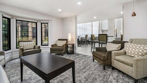 Ein modernes Wohnzimmer mit einer Couch, Sesseln, einem Couchtisch und einem Essbereich im Hintergrund.