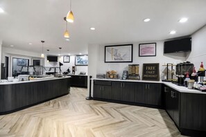 Cozinha moderna com bancada para refeições, armários de madeira e aviso indicando café da manhã diário gratuito.