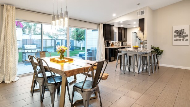 A modern kitchen with dark cabinets, a central island, and a dining area with a wooden table and metal chairs. - Preserve Oasis-Pool · Casita · Game Room · Treehouse (Phoenix)