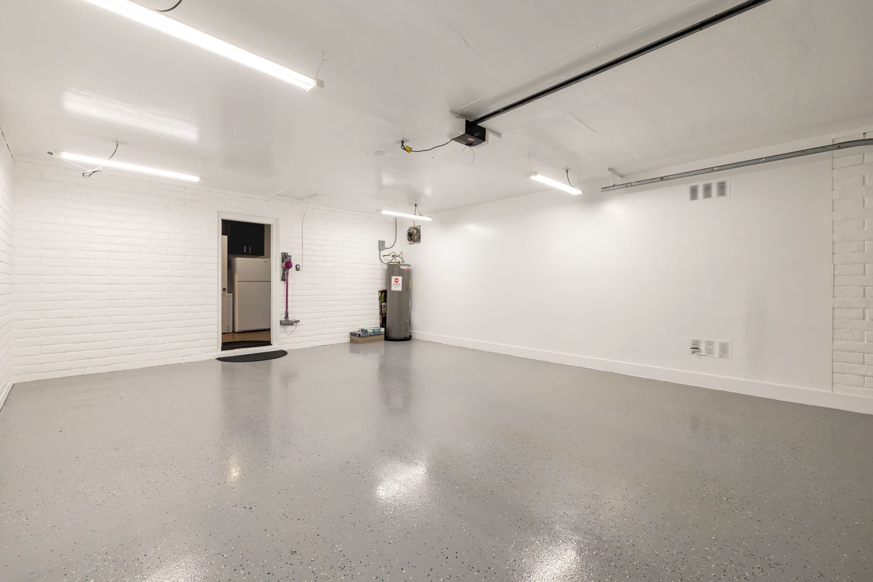 A spacious, well-lit room with white brick walls, a large industrial heater, and a door leading to another room.