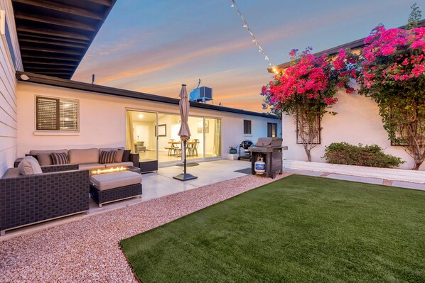 Un patio moderno con un sofá, una parrilla y luces colgantes.