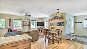 A spacious living room with a sofa, dining table, and chairs. There is a TV mounted on the wall and a ceiling fan. - Sunny Morristown Home - Walk to Restaurants! (Morristown)