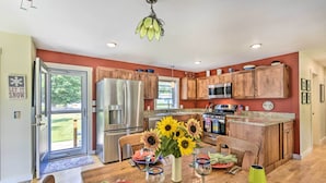 A modern kitchen with wooden cabinets, stainless steel appliances, and a dining area with a table set for four. - Sunny Morristown Home - Walk to Restaurants! (Morristown)