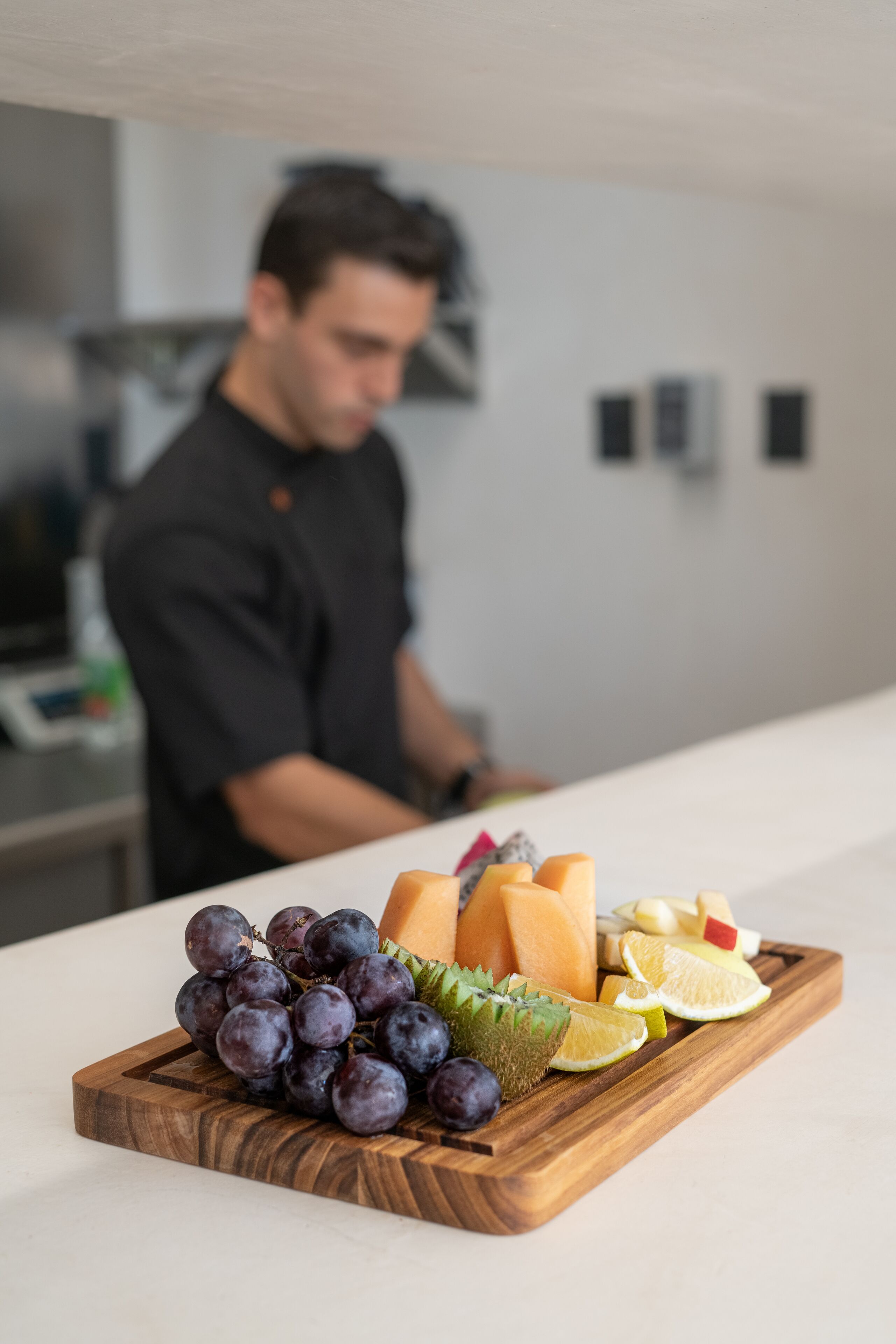 Una tabla de madera con frutas y verduras sobre una encimera de cocina.