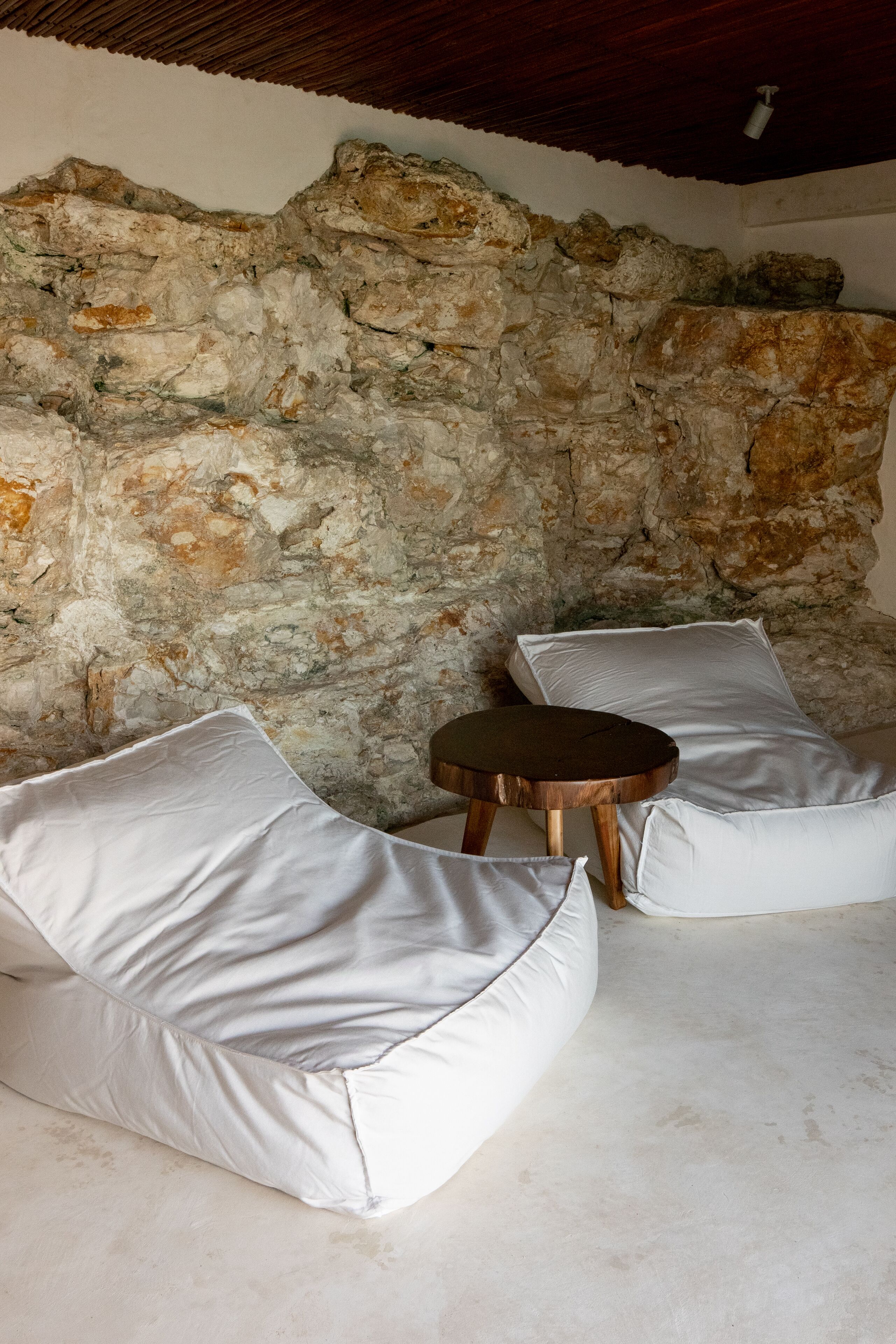 Un intérieur avec un mur en pierre, des sièges rembourrés blancs et une petite table en bois.