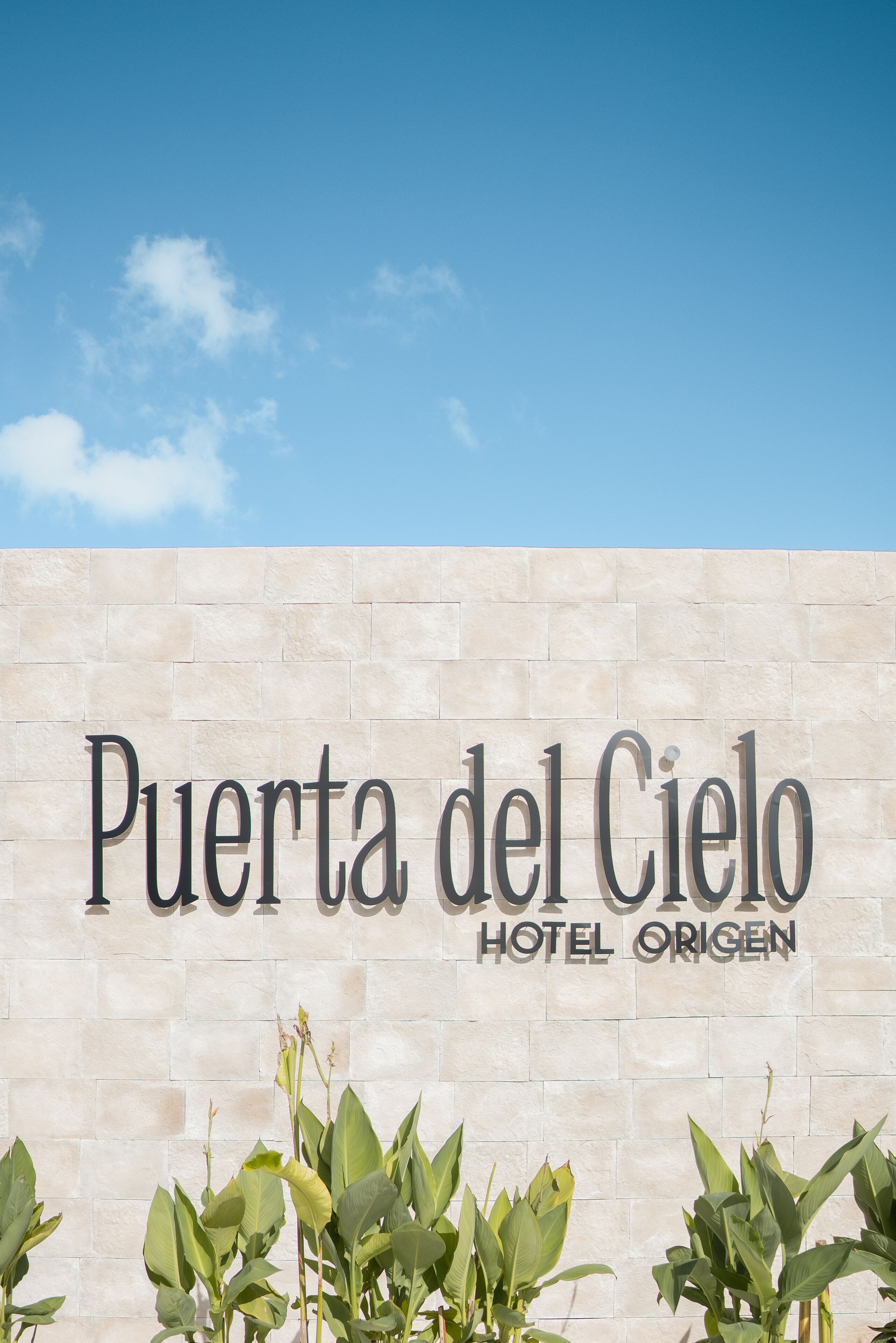 Un cartel para 'Puerta del Cielo Hotel Origen' con un cielo despejado al fondo.