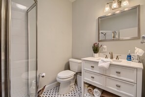 A bathroom with a glass shower enclosure, a toilet, a sink with a mirror above it, and a towel rack.