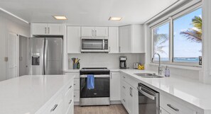 Prepare meals with ease in this kitchen featuring a refrigerator, microwave, and oven, with ample counter space and a window offering a view of the ocean.