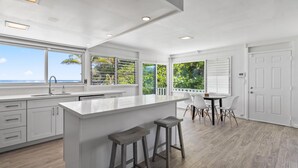A modern kitchen with a large island, white cabinetry, and a view of the ocean.