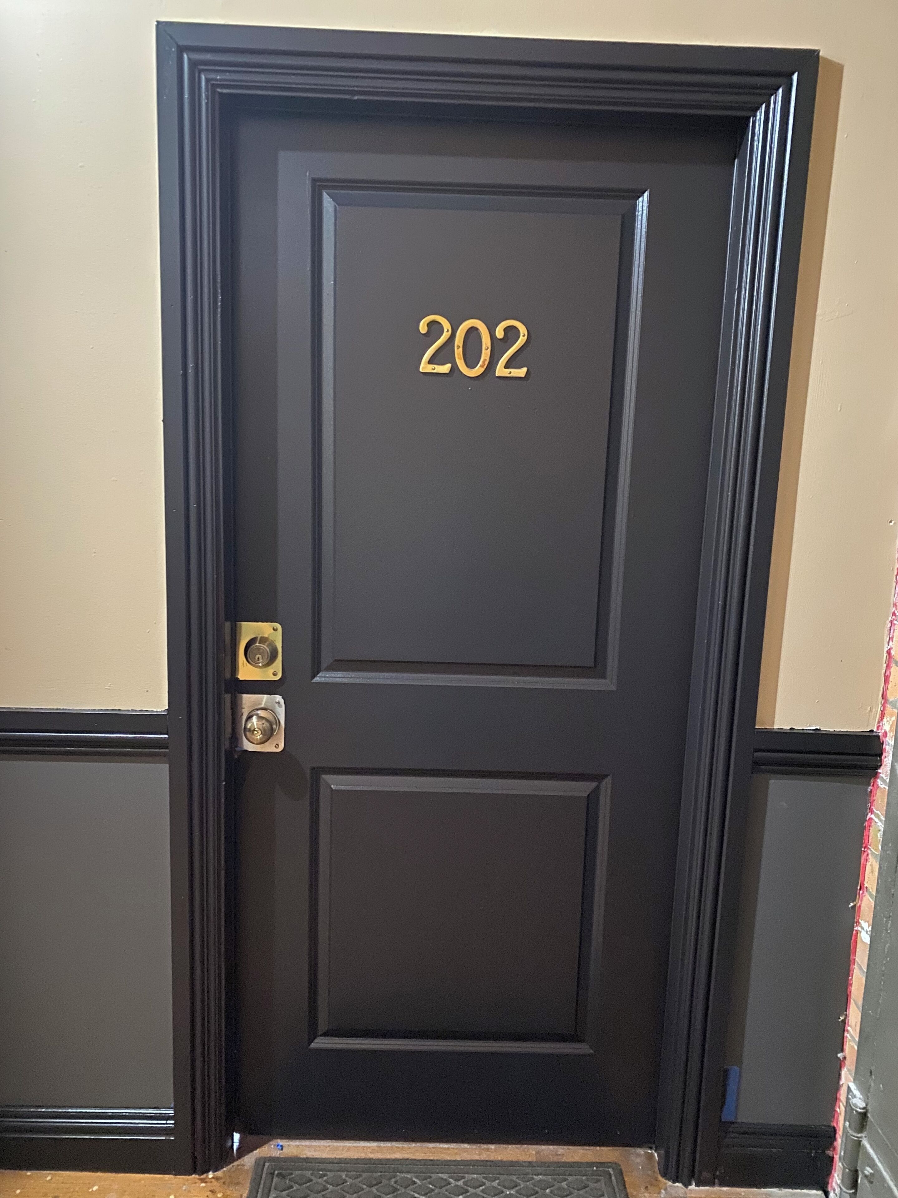 Una puerta de madera oscura con el número 202, un timbre de latón y un felpudo.
