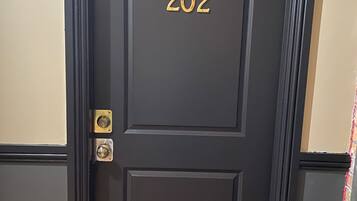 A dark wooden door with the number 202, a brass doorbell, and a doormat.